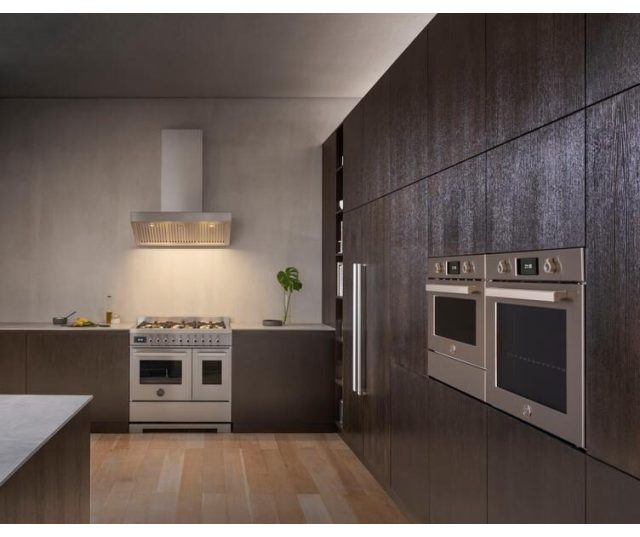 Bertazzoni PRO96L2EXT2 fornuis in keukenhoek naast twee ingebouwde ovens in donkere wandkasten