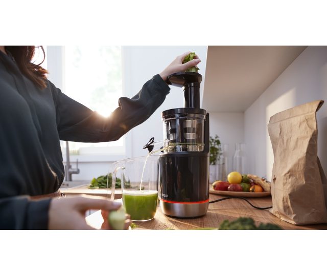 Gebruiker voert groen blad in toegangsopening Bosch MESM731M slow juicer