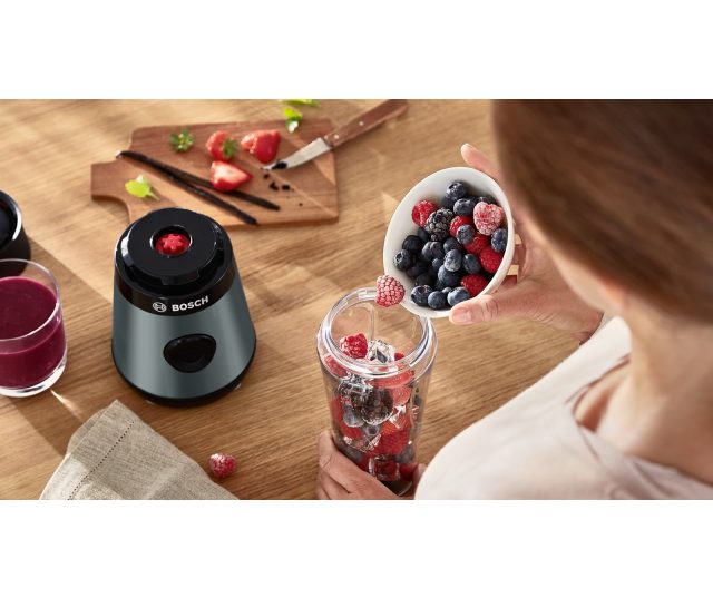 Bosch MMB2111S in gebruik met handen die vers bereid vruchtensap in mengbeker houden