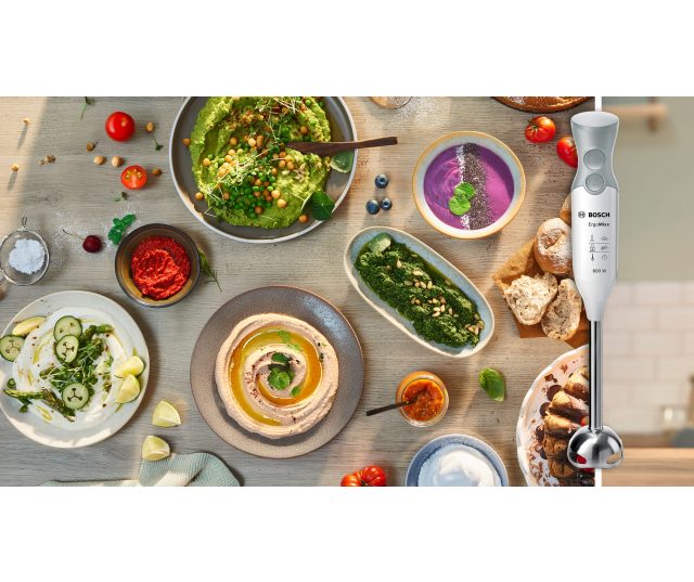Bosch MSM66110 staafmixer tussen diverse gerechten en ingrediënten op houten werkblad