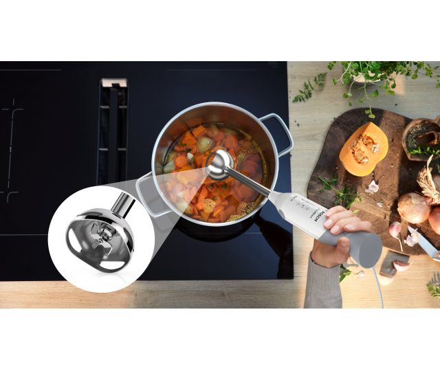 Close-up van mengvoet in werking in pan met groentebouillon op kookplaat