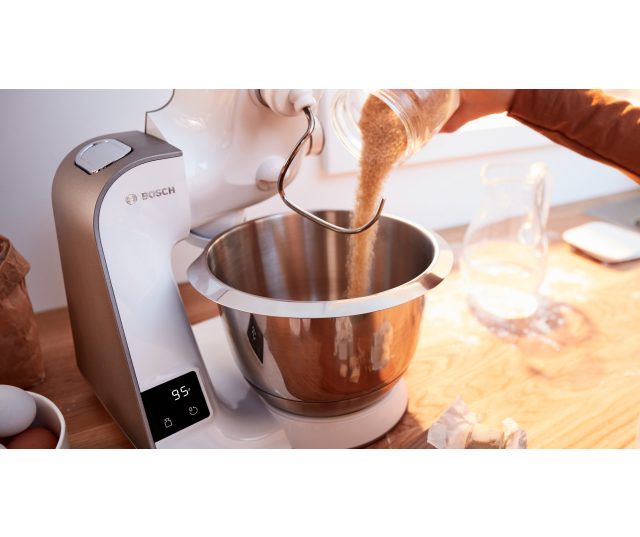 Bosch MUM5XW10 keukenmachine met mengkom en ingrediënten in gebruik, ingrediënt wordt toegevoegd