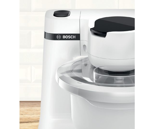 Bosch MUMS2AW01 keukenmachine zijaanzicht met merklogo en werkschaal gedeeltelijk zichtbaar op houten tafel