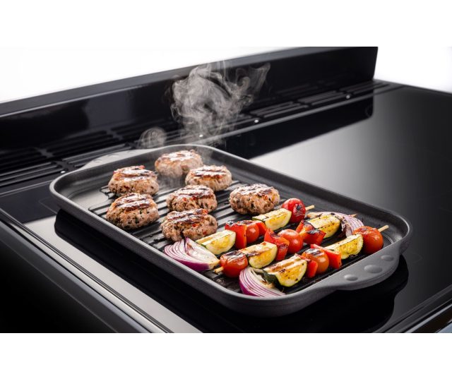 Inductiekookplaat bovenaanzicht met gegrilde hamburgers en groentespiesjes stoomend tijdens bereiding