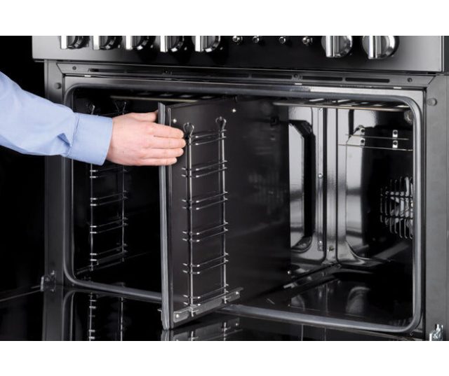 Geopende ovenruimte Falcon FXP 90 Gas links met uittrekbare rooster en hand die deur vasthoudt