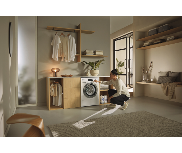 Miele WEG888 WCS in houten meubel met vrouw die de deur opent in moderne wasruimte