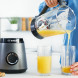 Bosch MMB6172S blender in gebruik, geel sap wordt uit glazen kan in glas gegoten op keukenblad